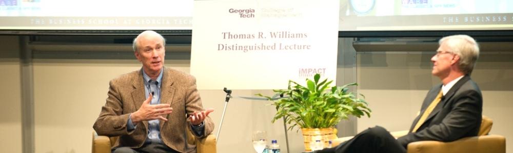 tWO GENTLEMEN SITTING ON STAGE FOR LECTURE